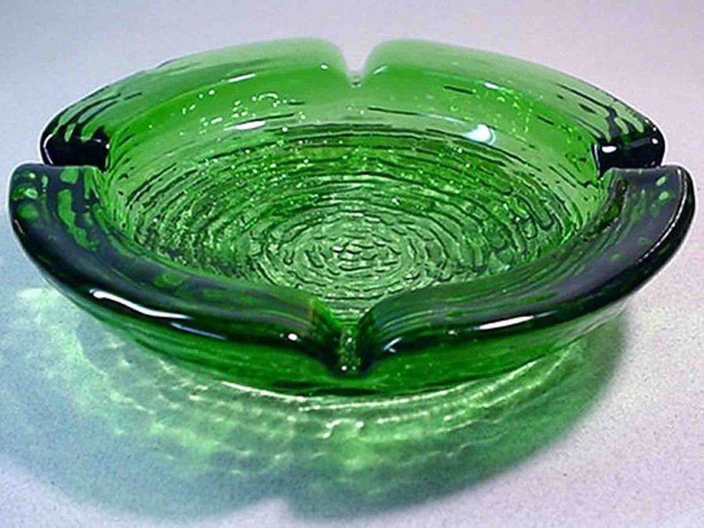  A green textured glass ashtray with two resting places for cigarettes.